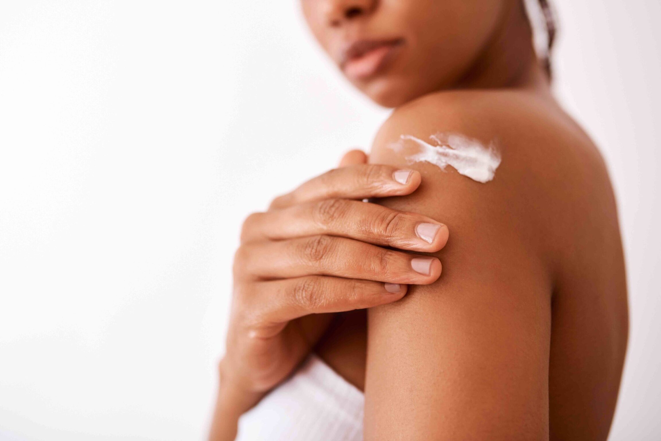 Studio shot of an unrecognizable woman with a darker complexion putting moisturiser on her body