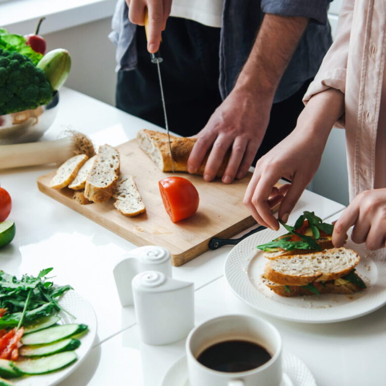 Two people chopping vegetables for sandwiches in their kitchen