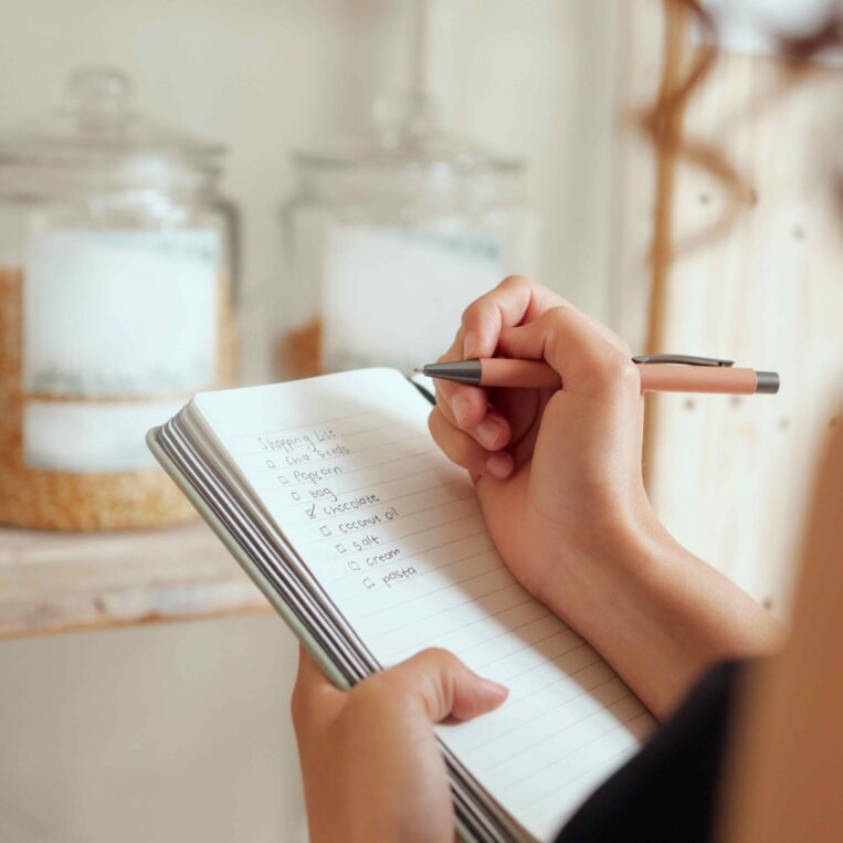Woman making shopping list for groceries on a notebook to plan a meal for dinner.