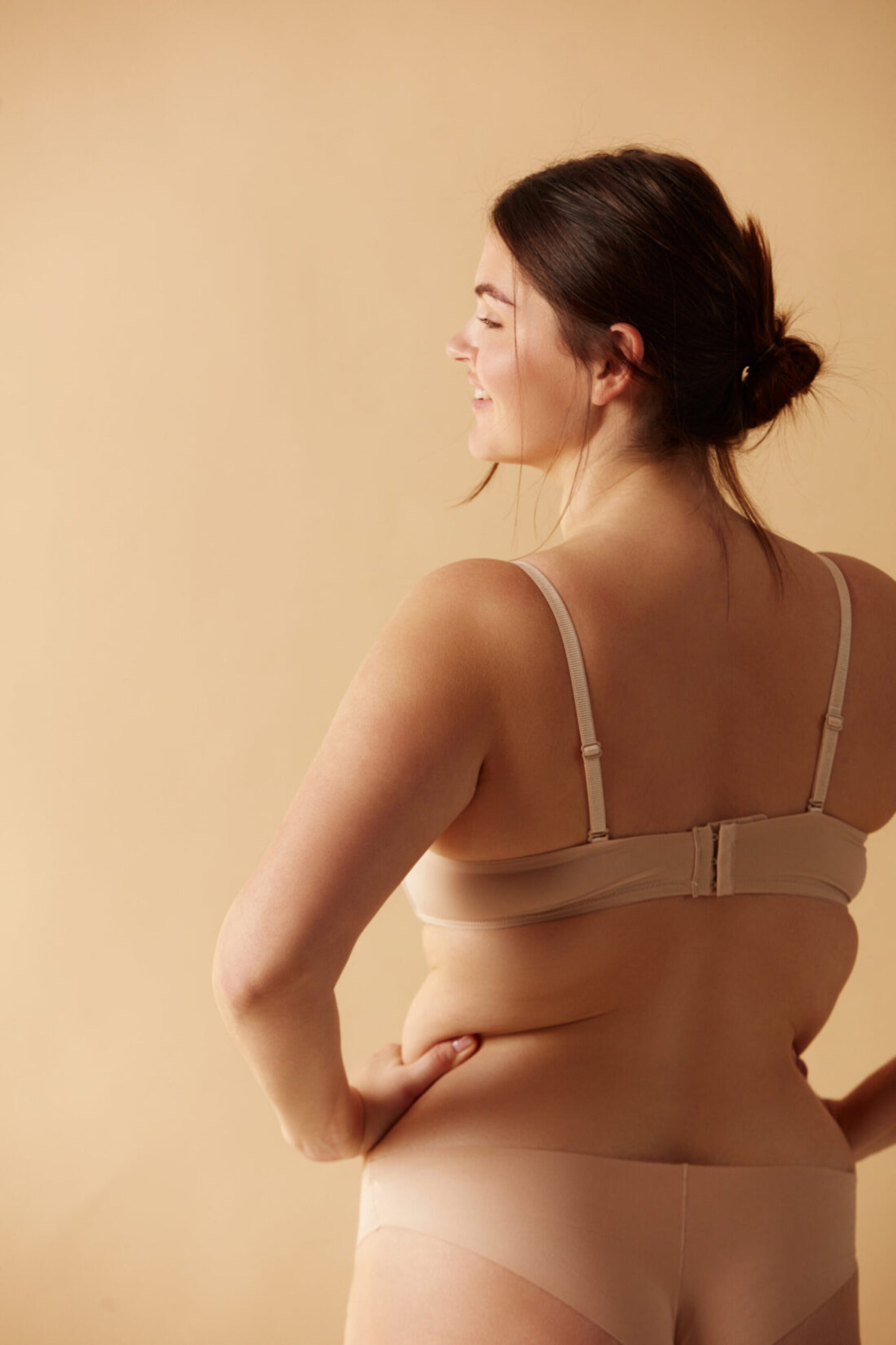 Recent Mommy Makeover patient posing in a room with muted colors and light