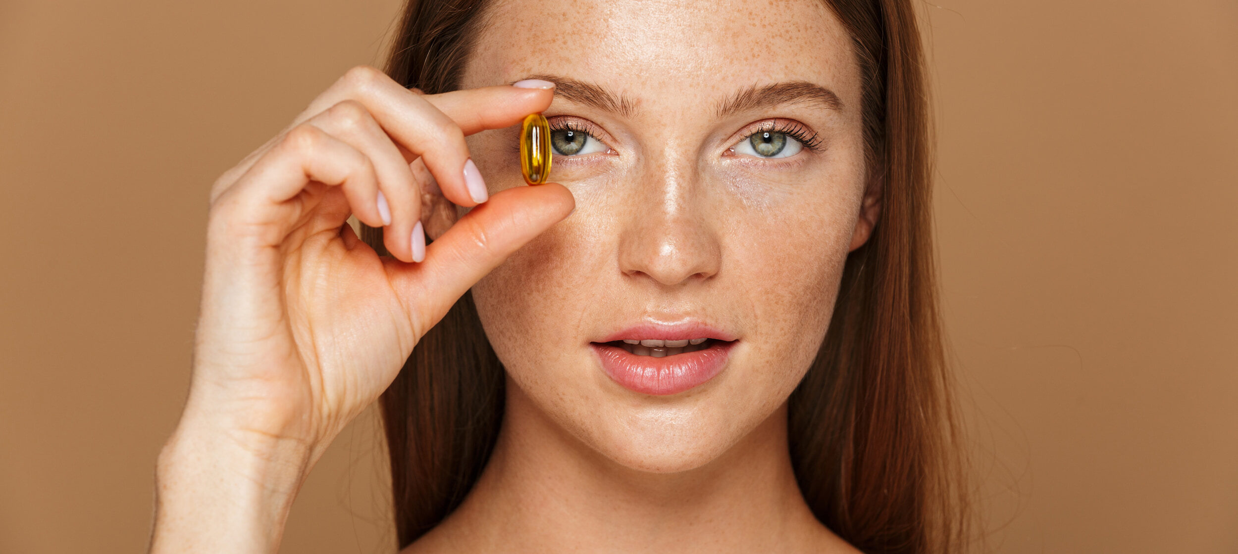 Woman holding a supplement close to her face with a muted brown background