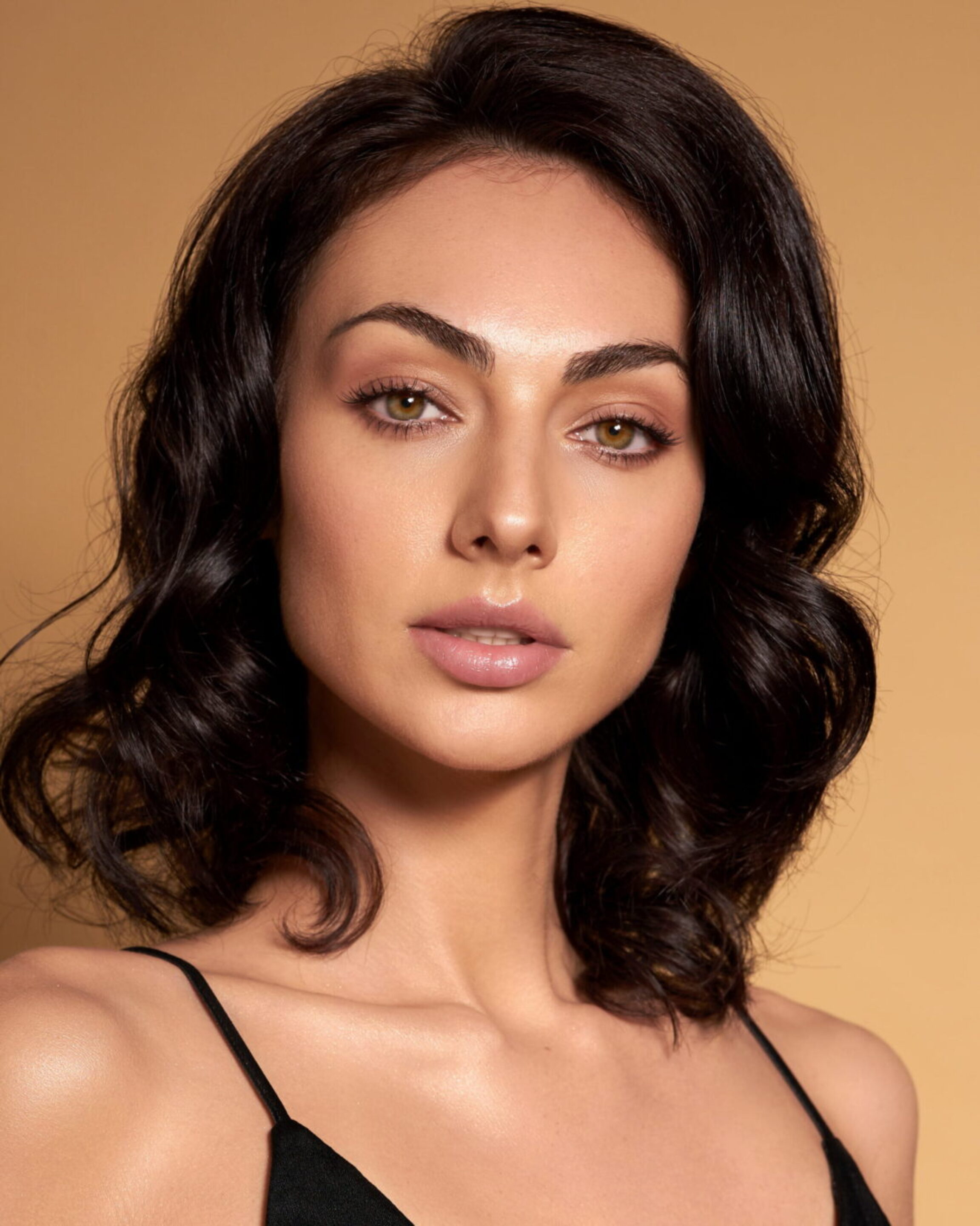 A woman with a slimmer jawline posing against a muted, golden brown background