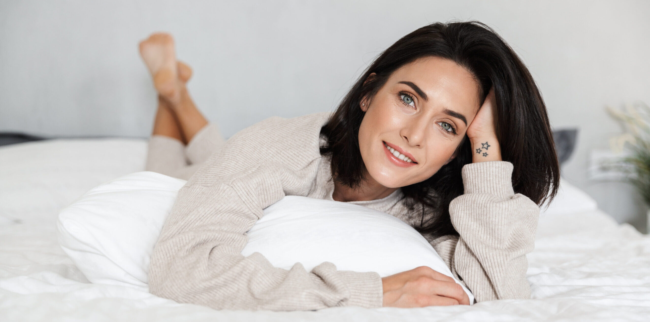 A well-rested millennial patient in her large bed, smiling at the camera