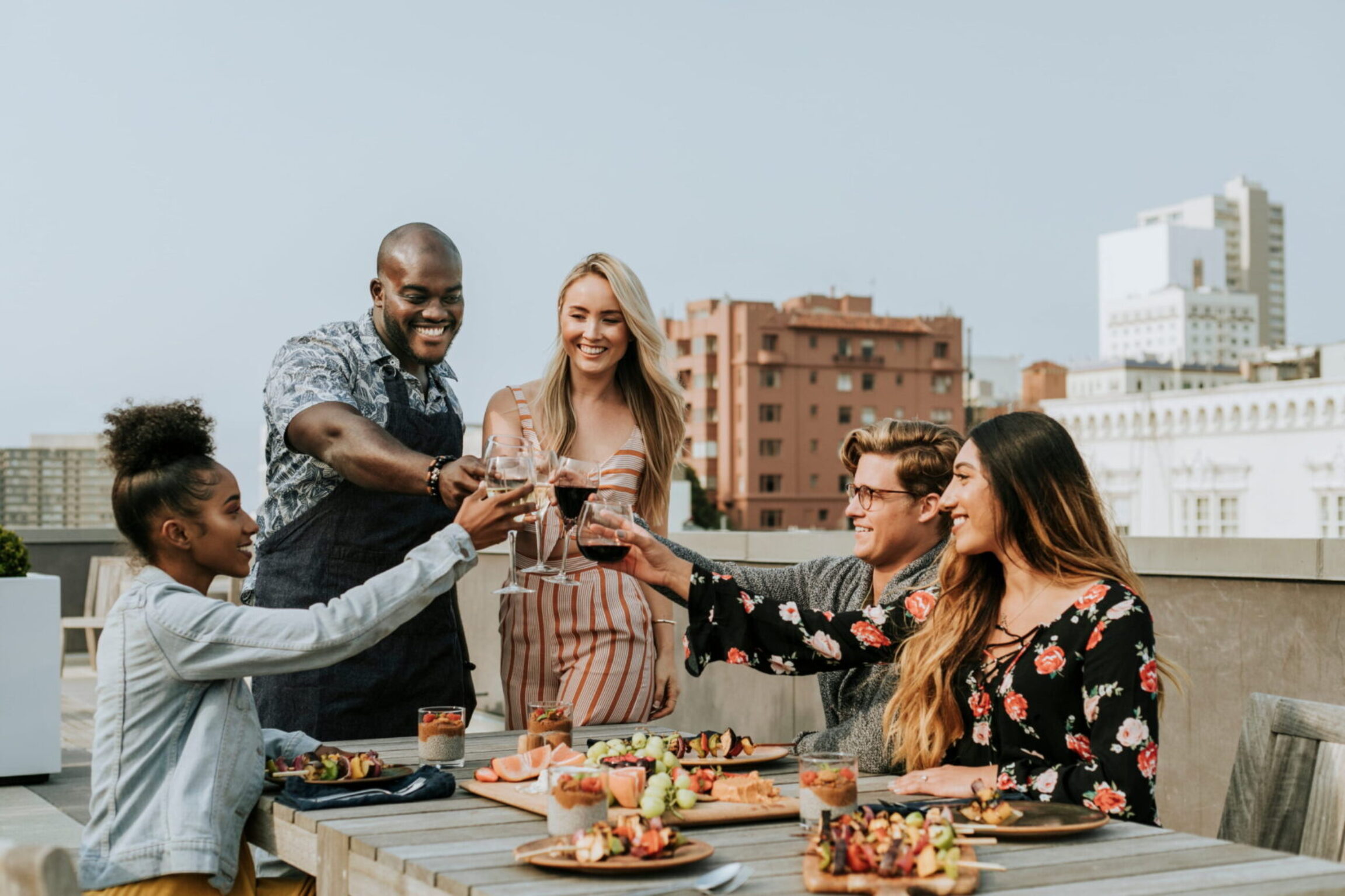 A photo of friends having alcoholic beverages at a rooftop dinner party in the city