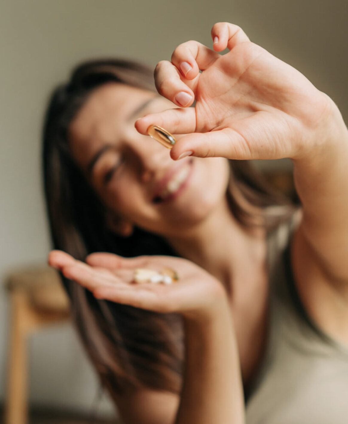 A late-20s functional medicine patient holding a fish oil pill close to the camera