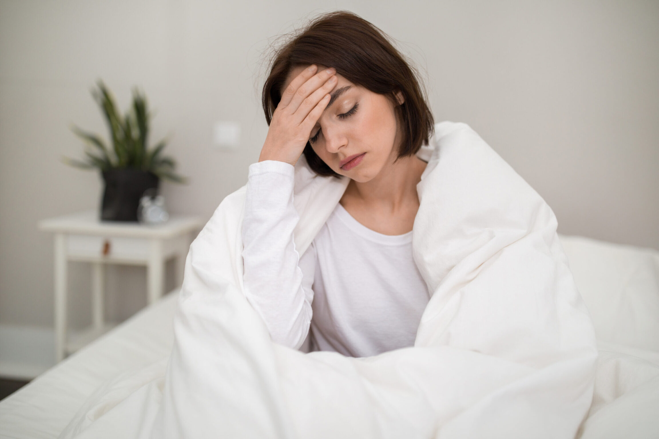 A woman sitting up in bed struggling to balance work stress and proper sleep