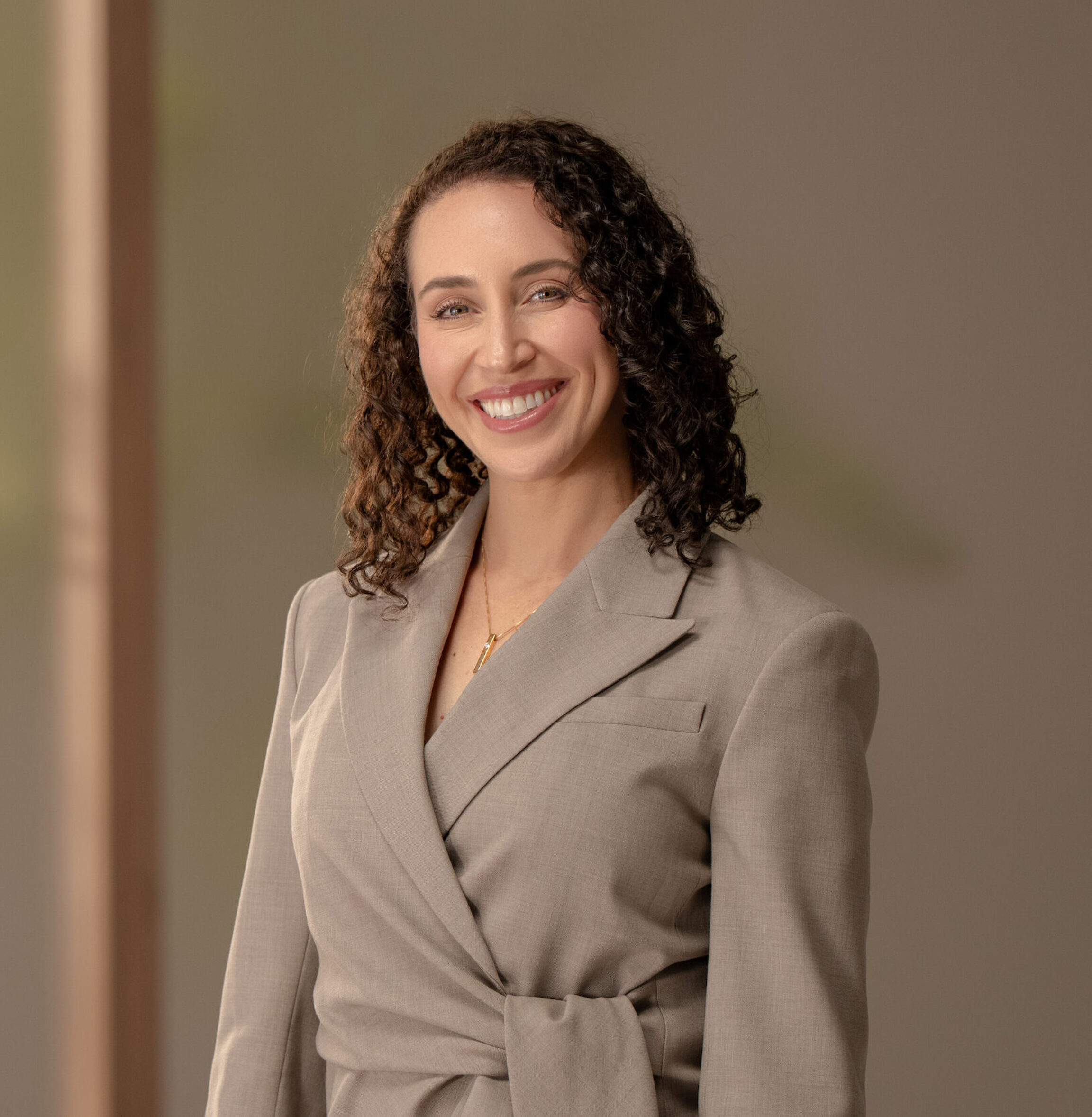 Dr. Michelle Sieffert posing for a photo in a muted suit against a brown background